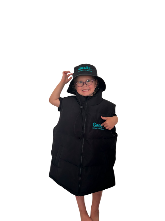 Young child wearing oversized branded puffer vest and bucket hat with Gear Uniforms + Promotions logo, smiling and posing confidently.